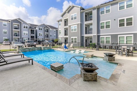 A swimming pool with a slide and a hot tub in front of apartment buildings.