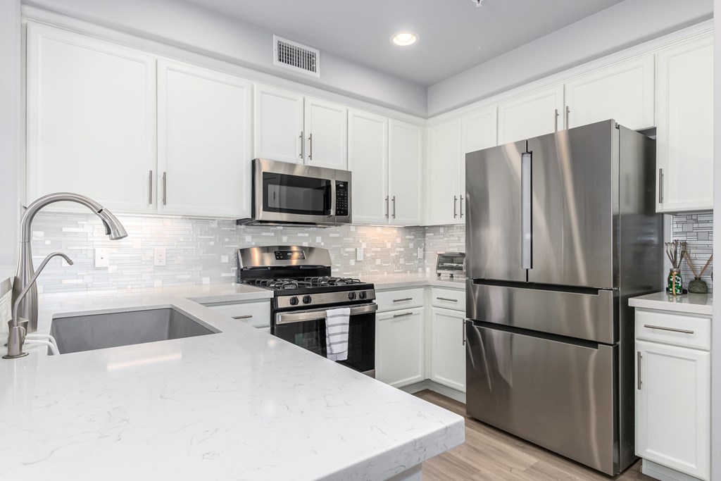 A modern kitchen with a stainless steel refrigerator and white cabinets.