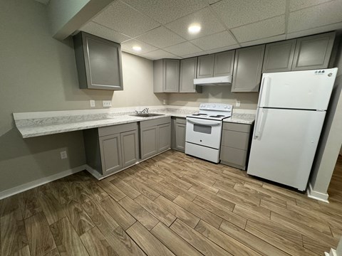A kitchen with a white fridge, white countertops, and wooden floors.