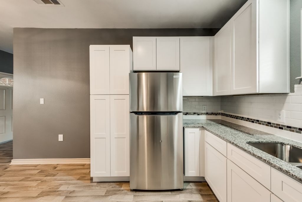 A modern kitchen with a stainless steel refrigerator and white cabinets.