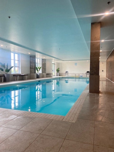 A large indoor swimming pool with a tiled floor and a high ceiling.