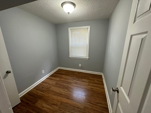 A room with a wooden floor and a window with blinds.