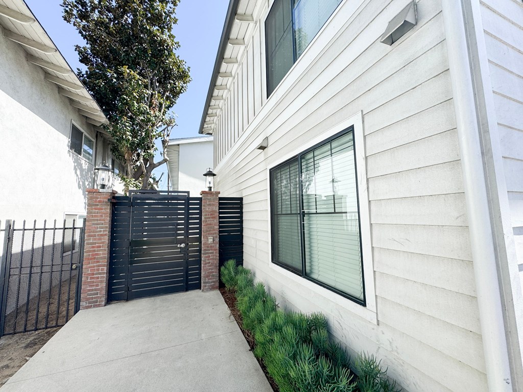 A white house with a black gate and a tree in front.
