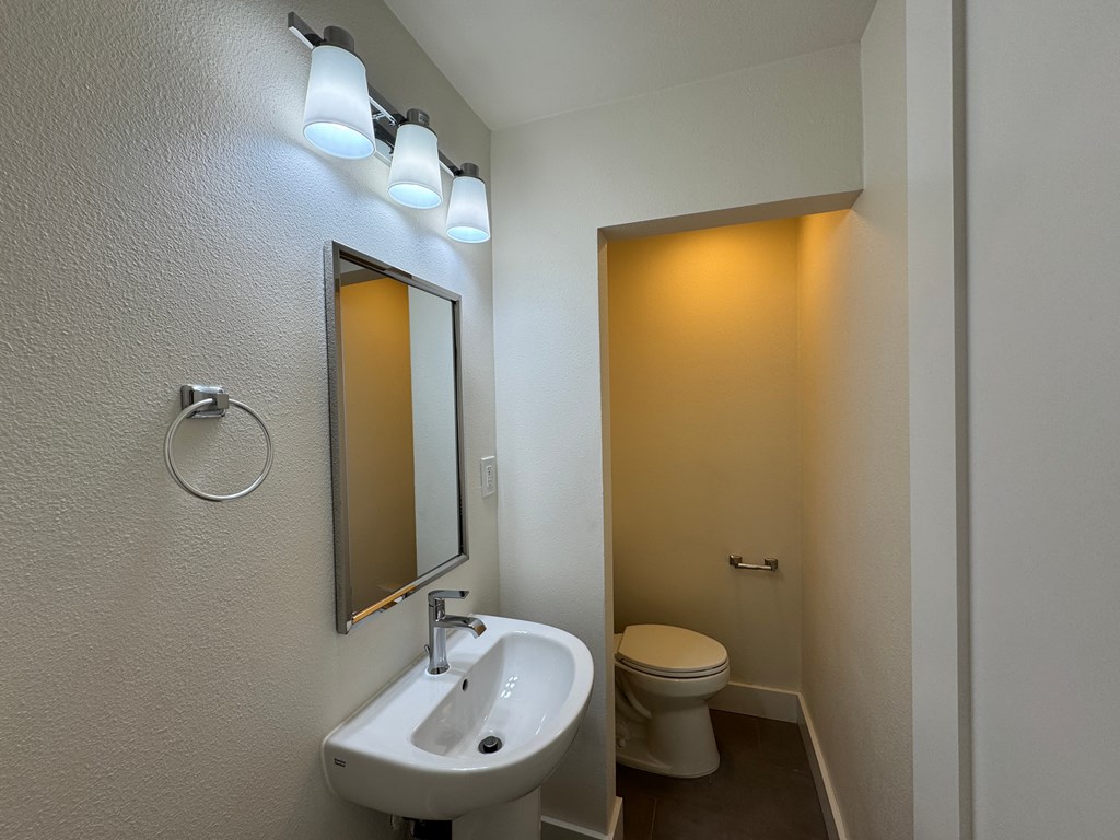 A bathroom with a sink, mirror, toilet and lights.