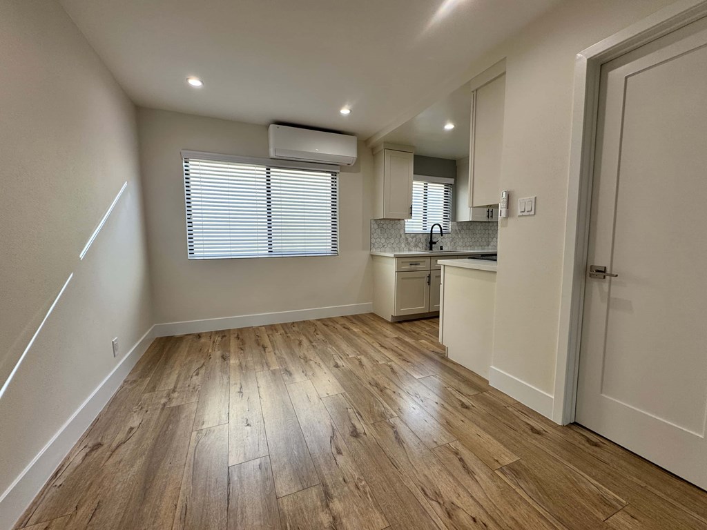 A room with wooden flooring and a kitchen area in the background.
