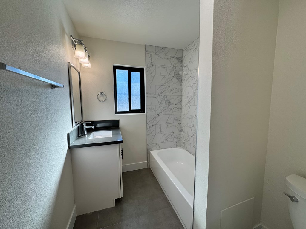 A small bathroom with a white tub and a window.