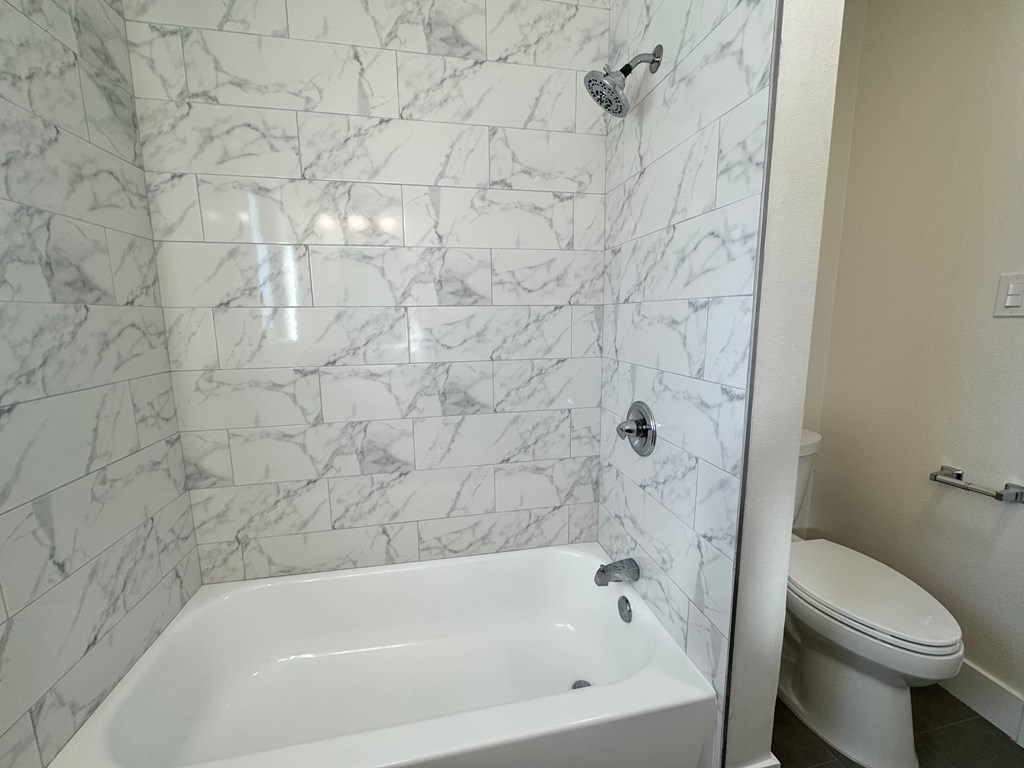 A white bathroom with a marble tile wall and a white tub and toilet.