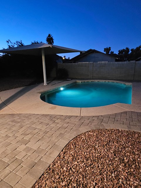 A pool surrounded by a stone patio and a gravel area.