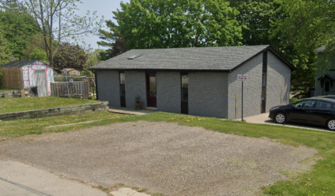 A small grey building with a black car parked in front.