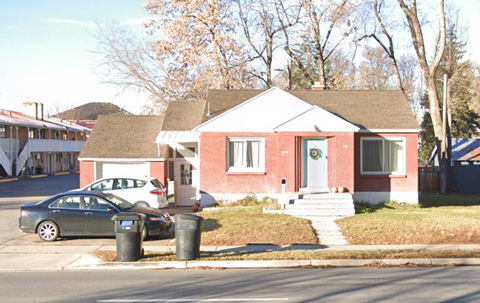 A red brick house with a green car parked in front.