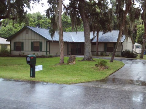 A wet road leads to a house with a green mailbox.