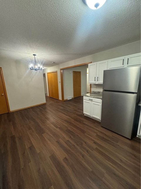 A kitchen with a refrigerator, cabinets, and a wooden floor.