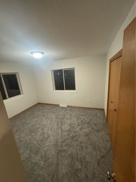 A room with a carpeted floor, a window, and a door.