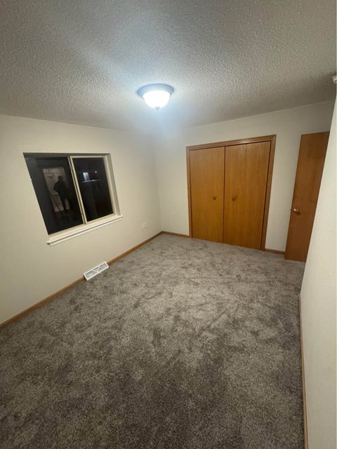 A room with a carpeted floor, a window, and two doors.