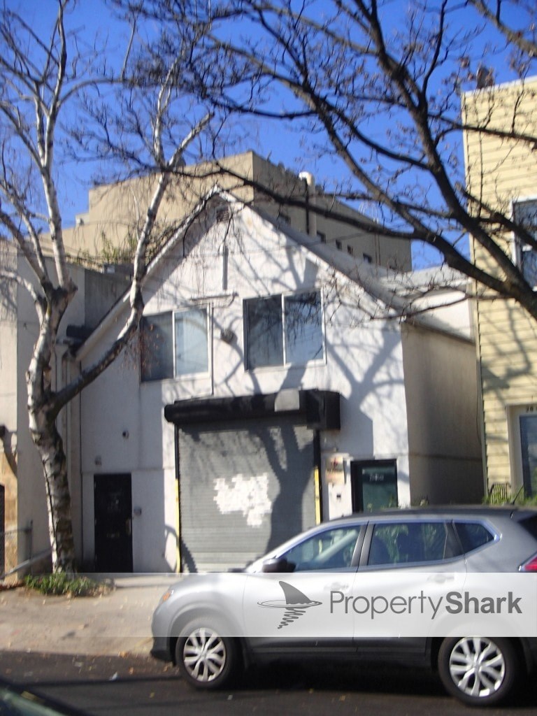 A silver car with PropertyShark written on the side is parked in front of a white building.