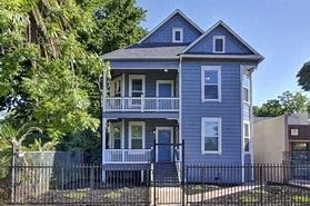 A blue two-story house with a porch and a fence.