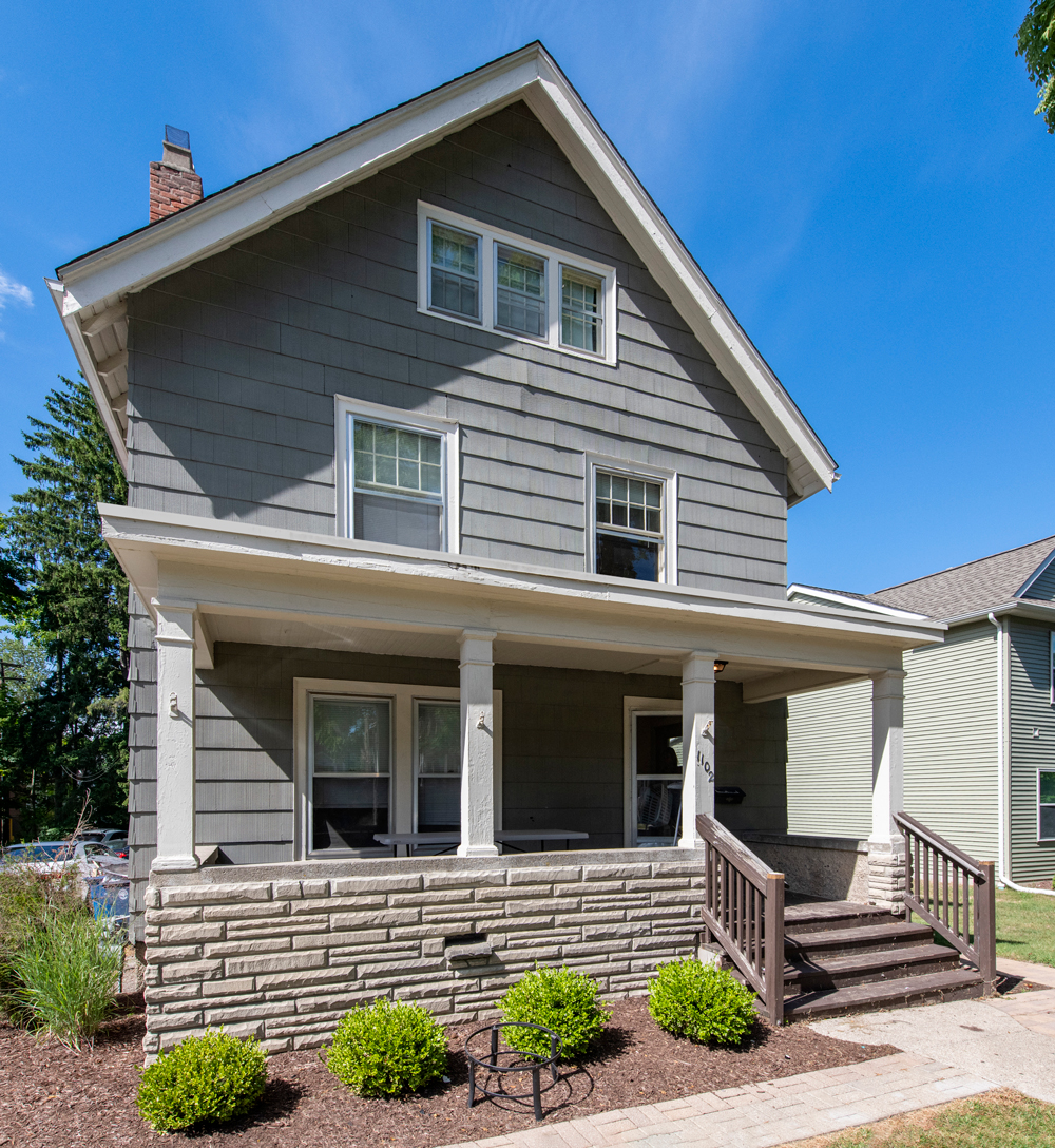 A house with a grey siding and a white porch.
