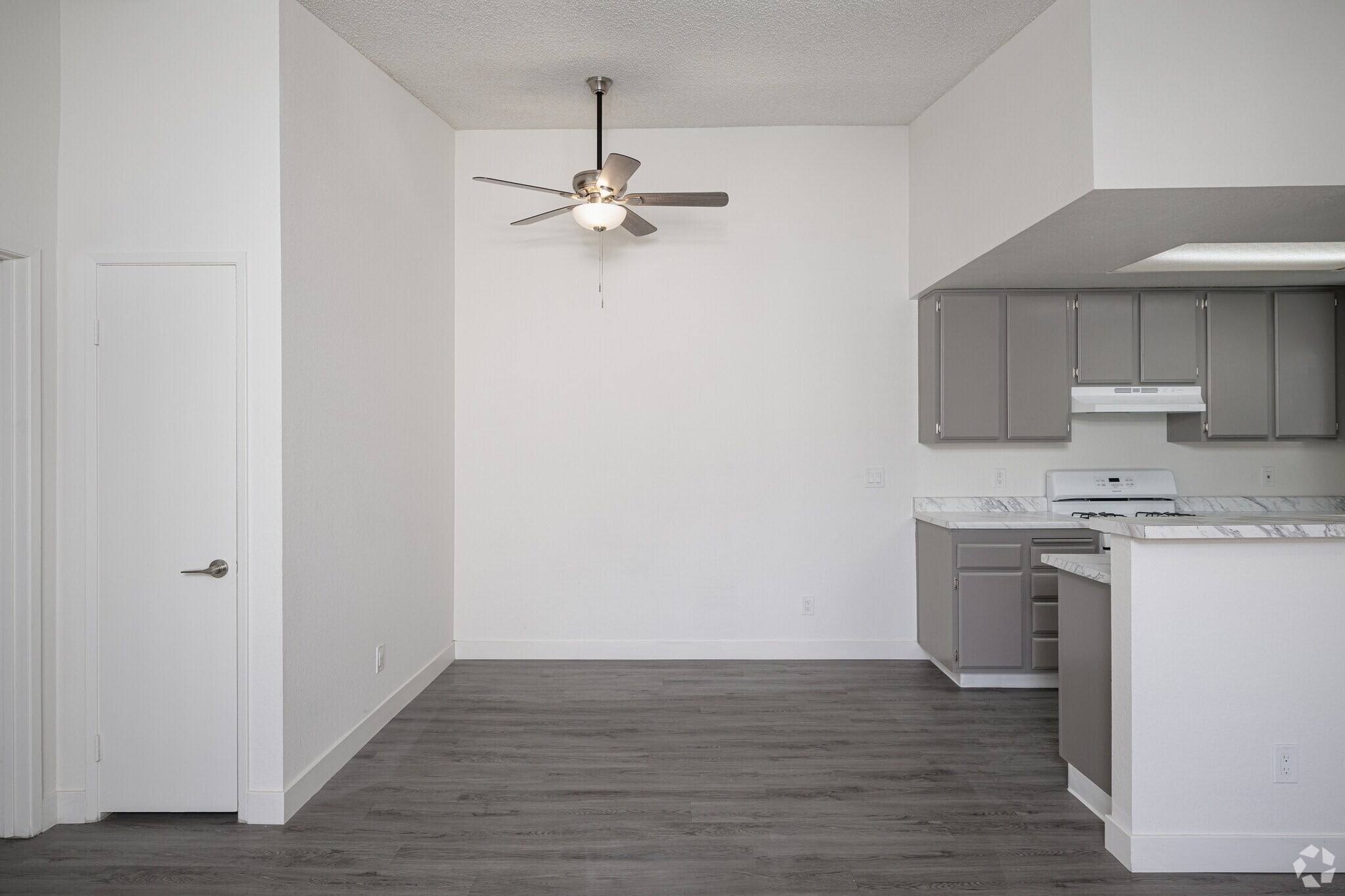 A white kitchen with a ceiling fan and a white door.