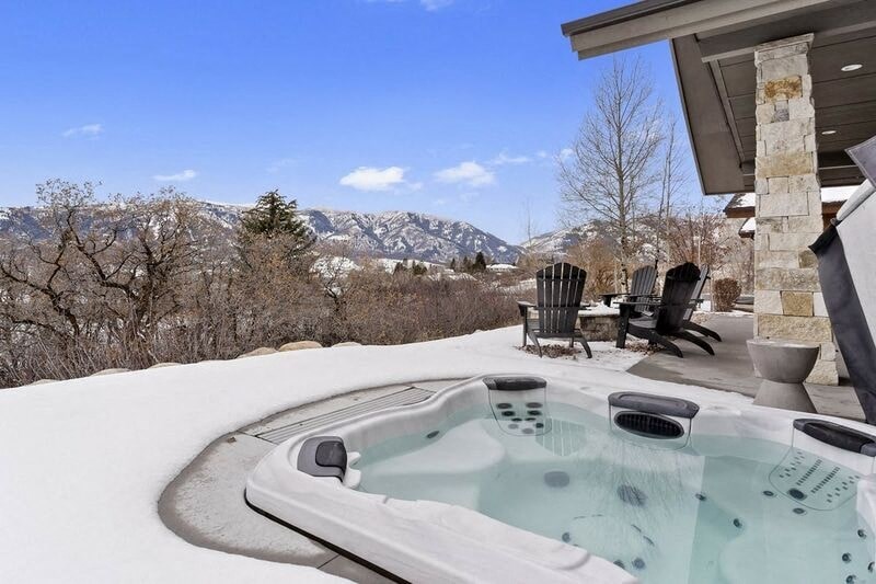 A hot tub sits in the snow with a mountain in the background.