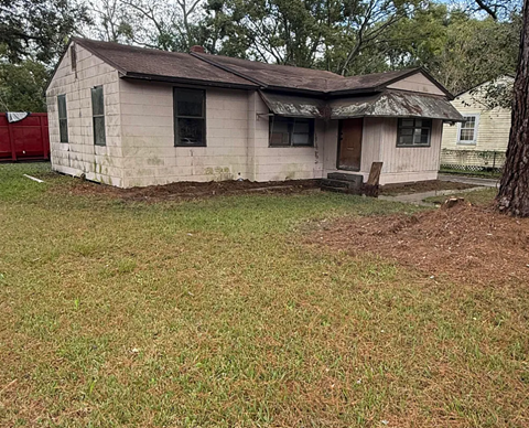 A small, old house with a brown roof and a dirt area in front.