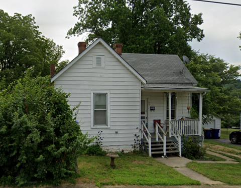 A small white house with a porch and a chimney.