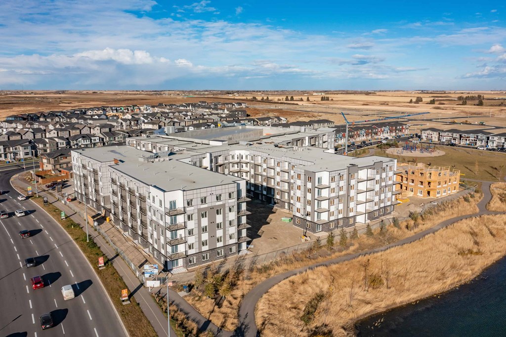 A large, modern apartment complex sits on a hillside with a road running alongside it.