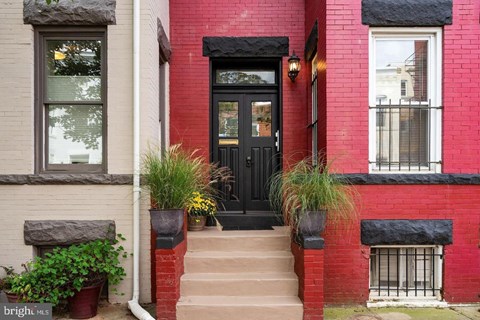 A red brick house with a black door and steps leading up to it.