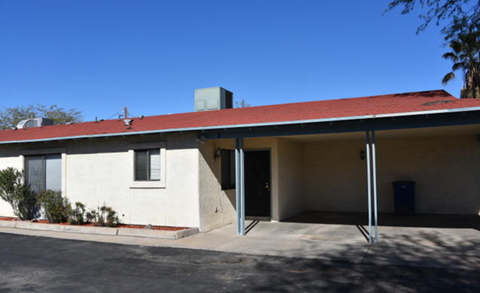 A white building with a red roof and a blue trash can in front.