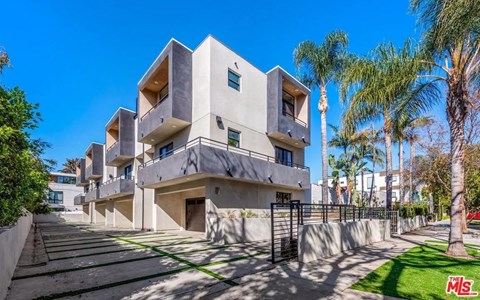 A modern building with a flat roof and balconies is surrounded by a well-manicured lawn and palm trees.