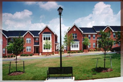 A black bench is in the middle of a grassy area in front of a building.