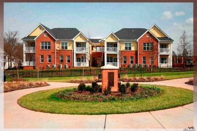 A red brick apartment building with a small garden in front.