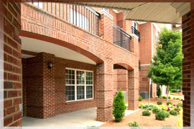 A red brick house with a balcony and a tree in the front yard.