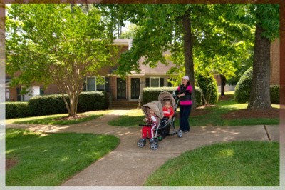 A woman with a baby in a stroller is walking in front of a house.