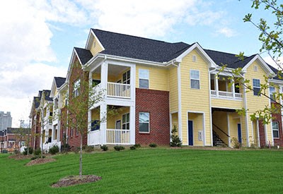 A yellow and red two story apartment building with a tree in front.