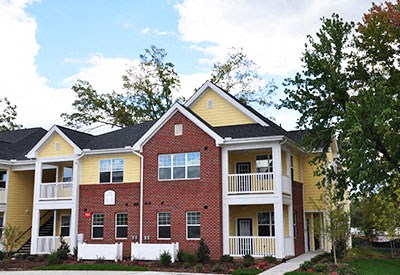 A yellow and red two story house with a white fence.