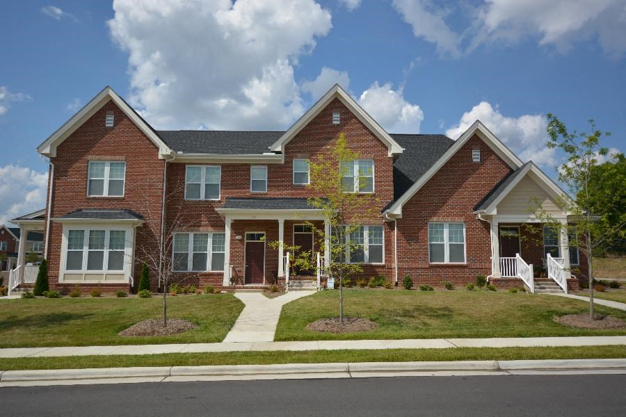 A large brick house with a front porch and a tree in front.