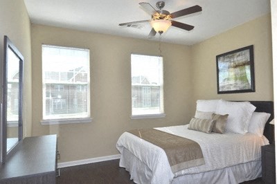 A bedroom with a bed, a ceiling fan, and two windows.