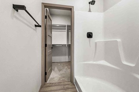 A white bathroom with a walk in shower and a doorway leading to a bedroom.