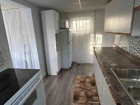 A kitchen with a black stove top oven, a white refrigerator, and a brown patterned rug on the floor.