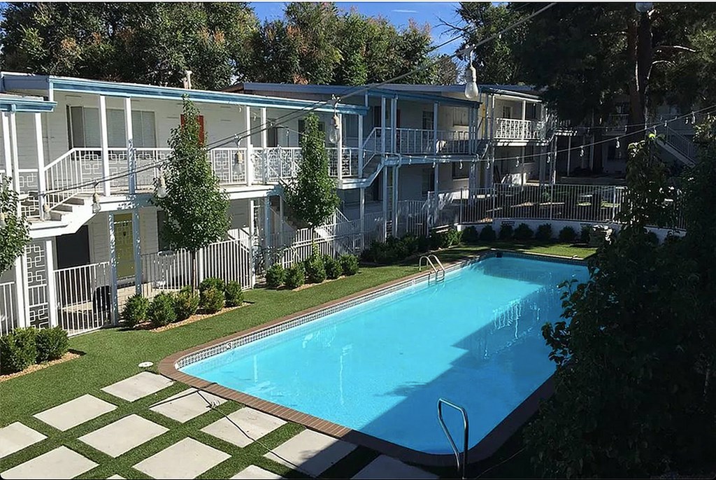 A swimming pool in front of a white building surrounded by trees.