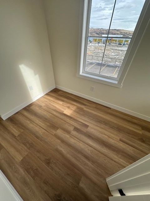 A room with wooden flooring and a window overlooking a parking lot.