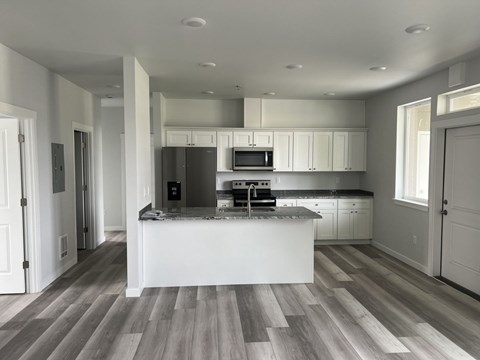 A kitchen with a black refrigerator, white cabinets, and a wooden floor.