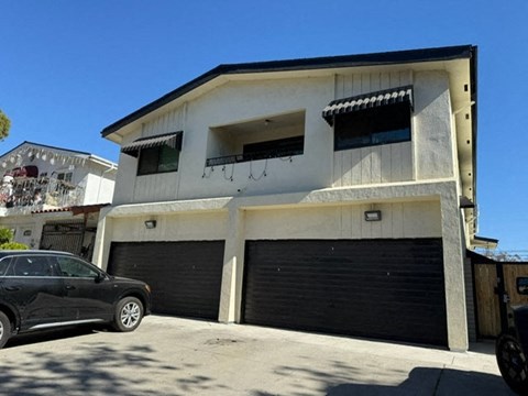 A black car is parked in front of a two-story house with a garage.