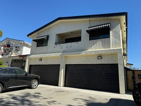 A black car is parked in front of a two-story building with a garage.