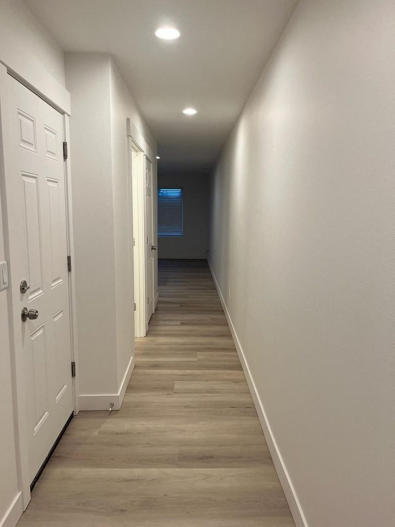 A long hallway with white doors and wood flooring.