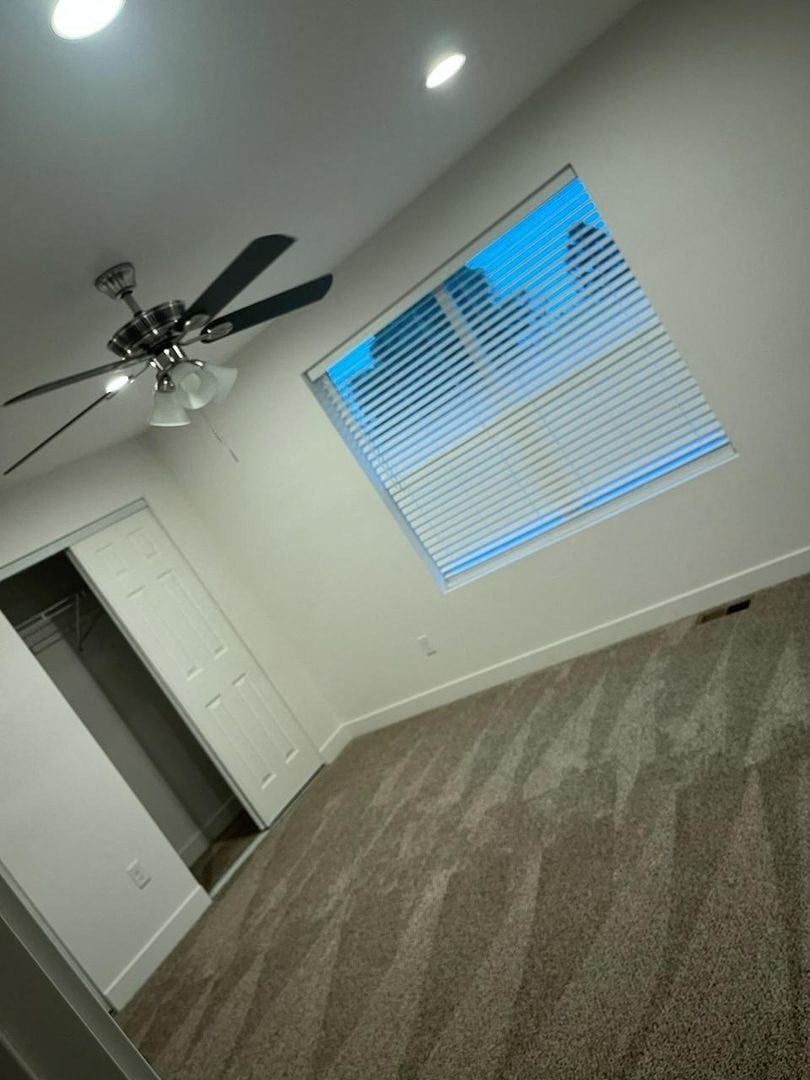 A room with a ceiling fan and a window with blinds.