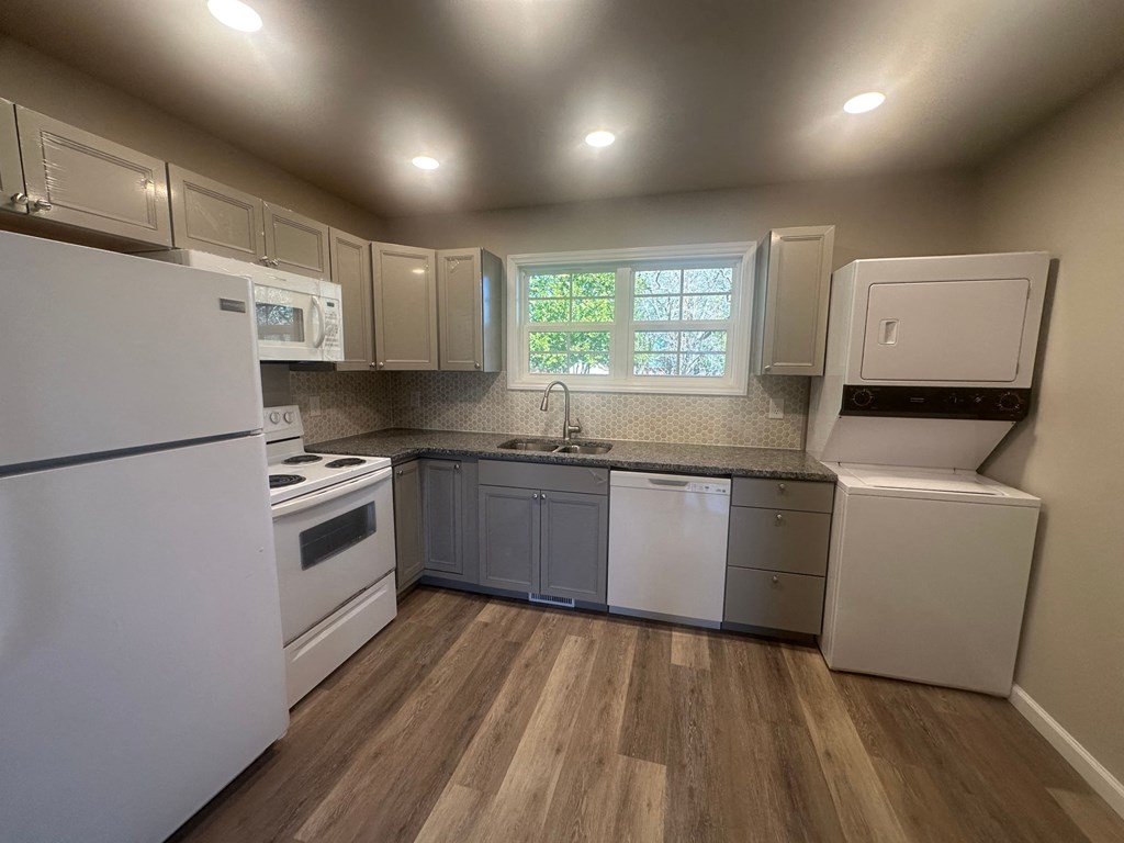 A kitchen with white appliances and wooden floors.