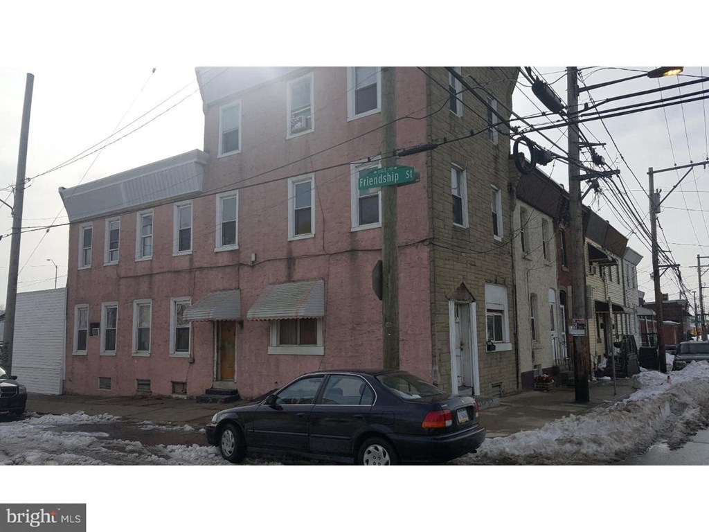 A black car is parked on the street in front of a pink building.