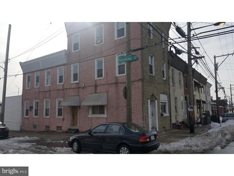 A black car is parked on the street in front of a pink building.
