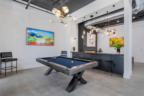 A pool table is in the middle of a room with a chair and a painting on the wall.